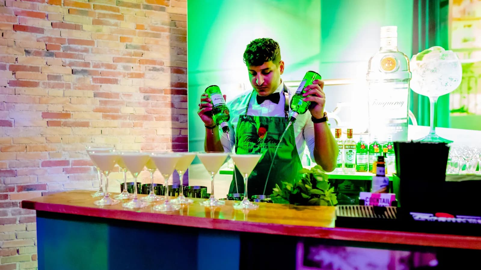 Bartender i grønt scenelys der shaker drinks bag en oplyst bar